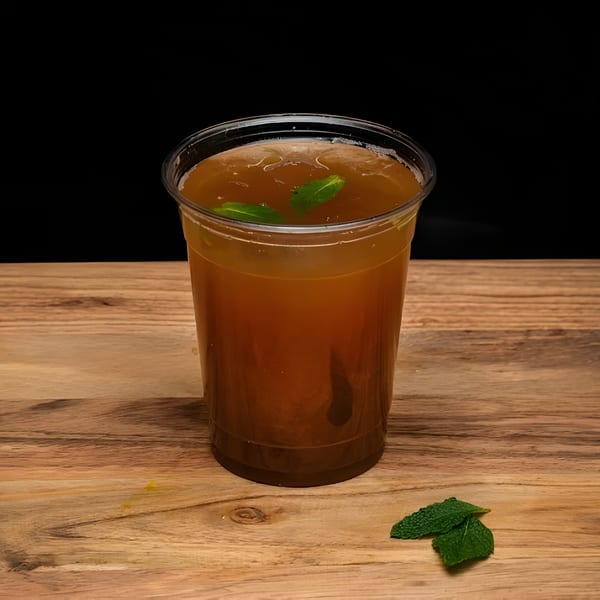 A refreshing iced tea with mint leaves in a clear plastic cup on a wooden surface.