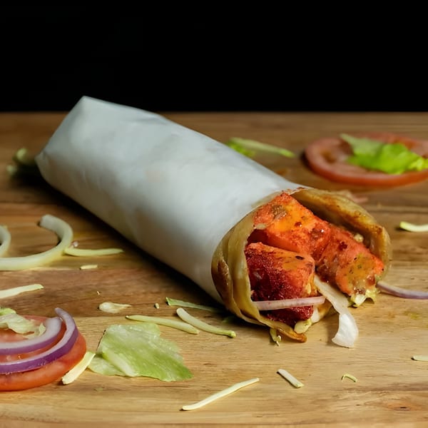 A halal chicken tikka roll, partially unwrapped, on a wooden board with scattered vegetables.