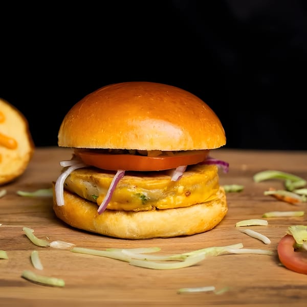 A halal Food Street burger with a golden bun, cheese patty, tomato, and red onion on a wooden board.
