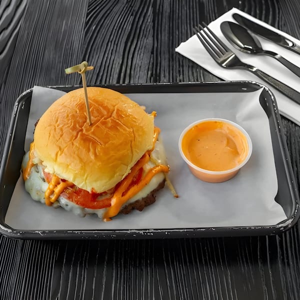 A halal burger with melted cheese, red peppers, and orange sauce, served with a side of sauce.