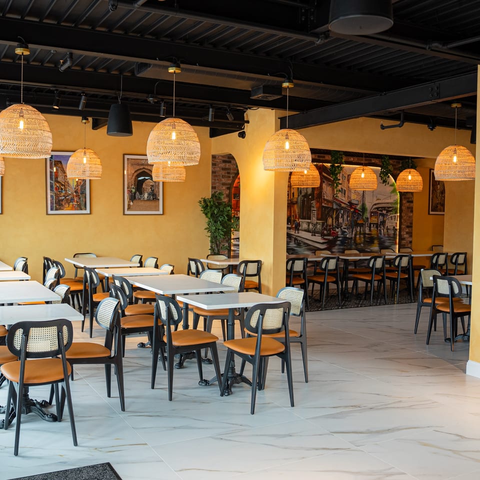 Spacious restaurant dining room with yellow walls, rattan pendant lights, and black and tan chairs.