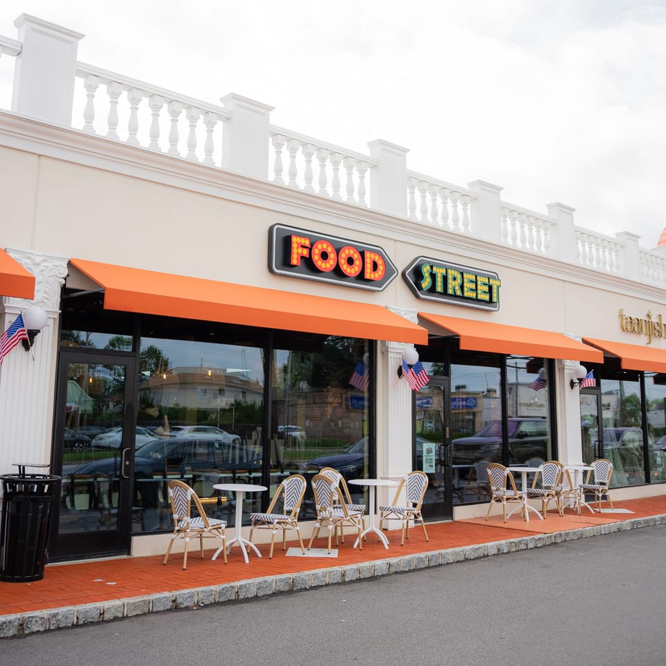 Food Street restaurant exterior with orange awnings, outdoor seating, and a neon sign.